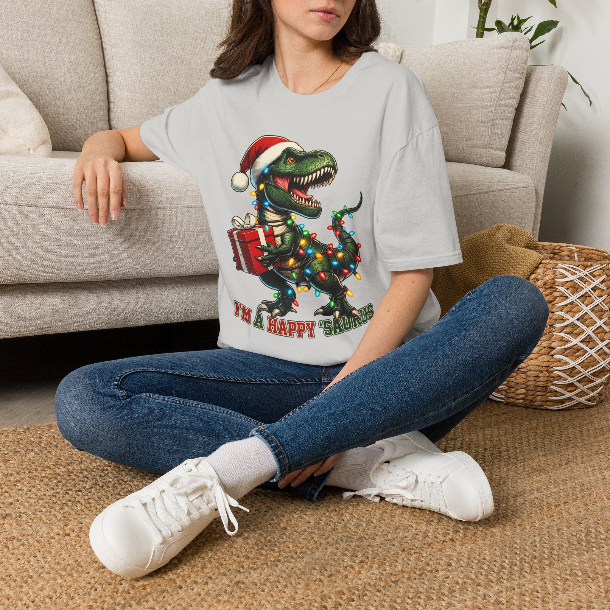 Happy Saurus T-Rex Santa Hat Christmas Lights t-shirt in Ice Grey, worn by a woman seated on a rug