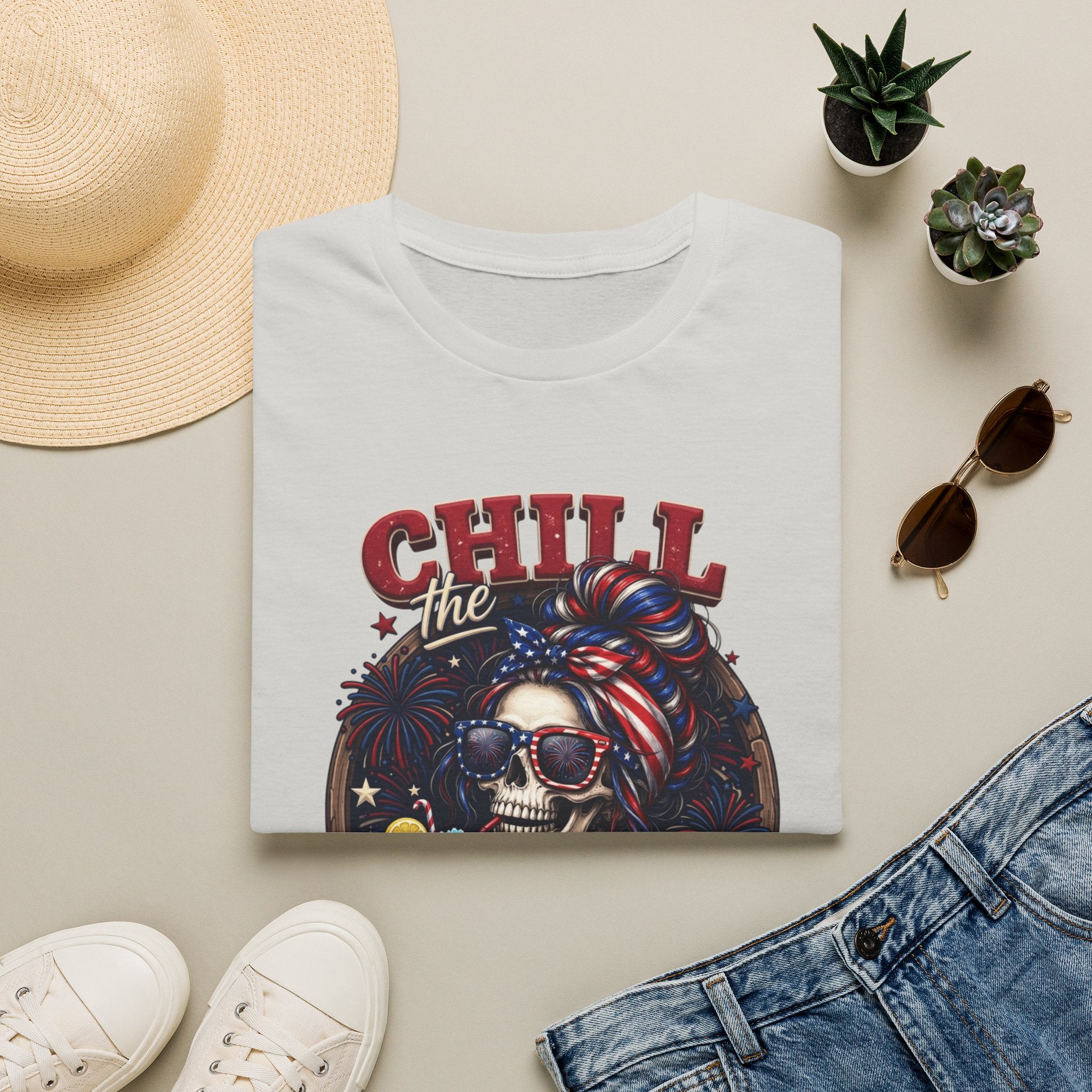 Chill the Fourth Out Patriotic Skeleton 4th of July print on an Ice Grey t-shirt, folded beside a straw hat and jeans