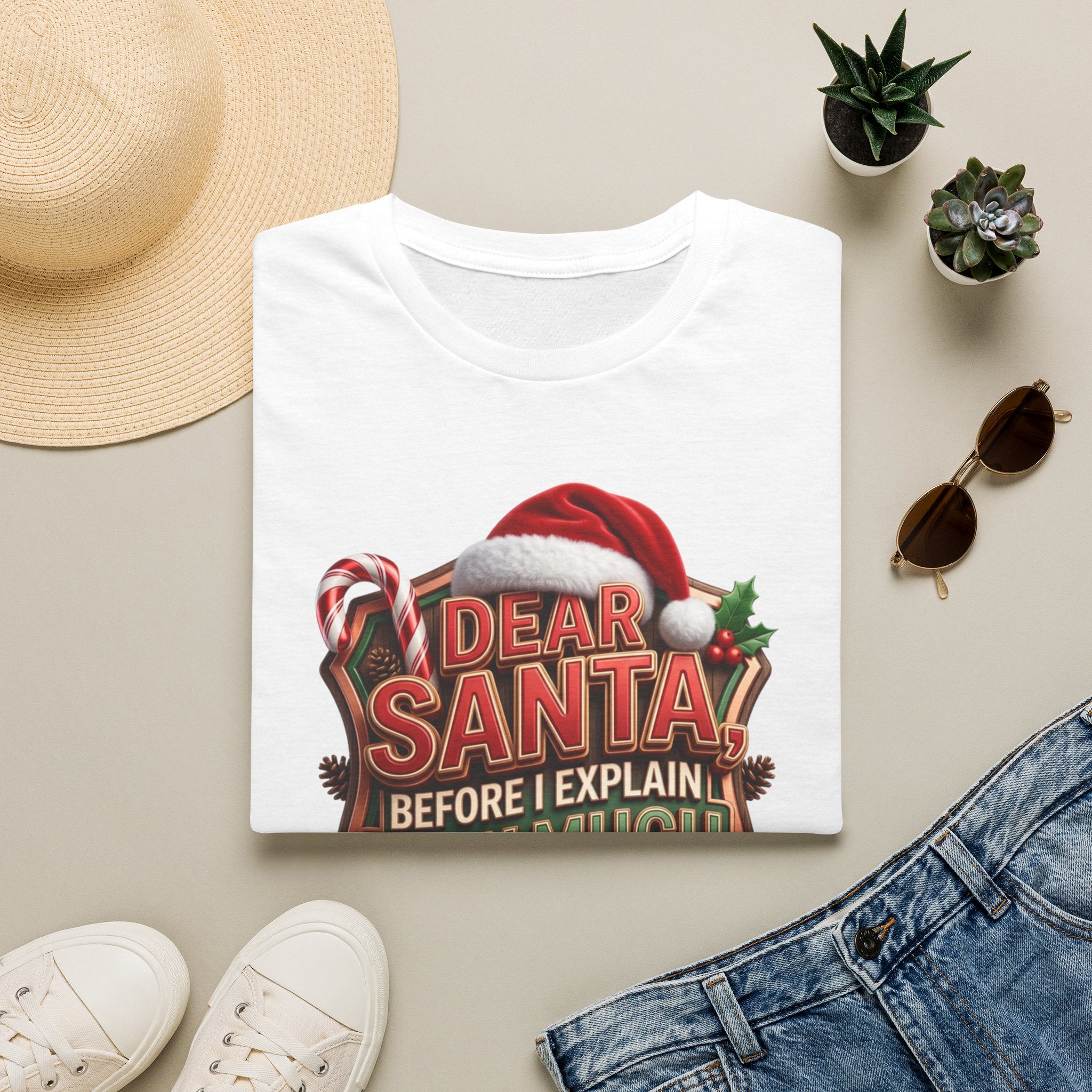 Dear Santa Before I Explain print on a White t-shirt, folded beside a straw hat and jeans