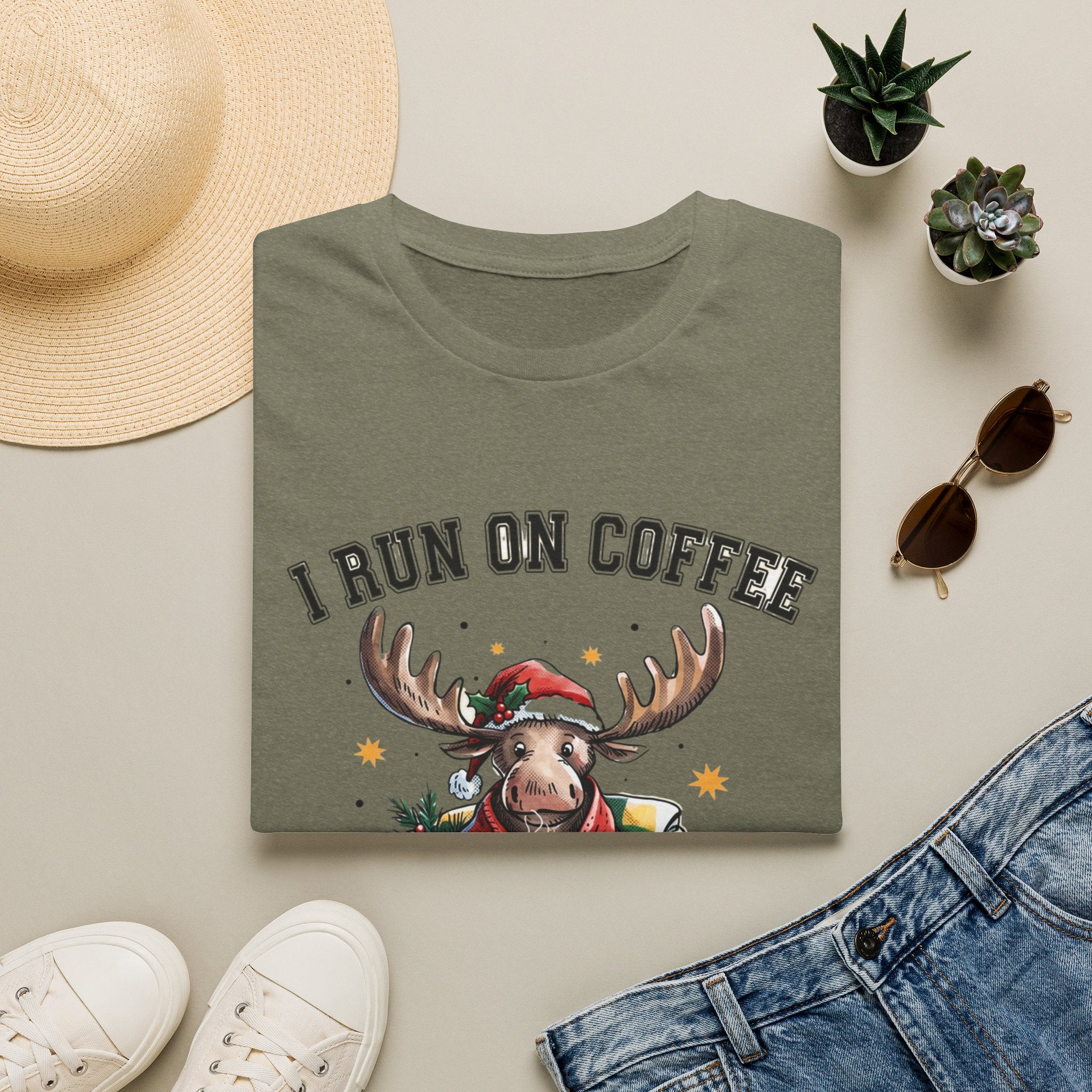 Moose I Run On Coffee and Sleighin' It print on a Heather Military Green t-shirt, folded beside a straw hat and jeans