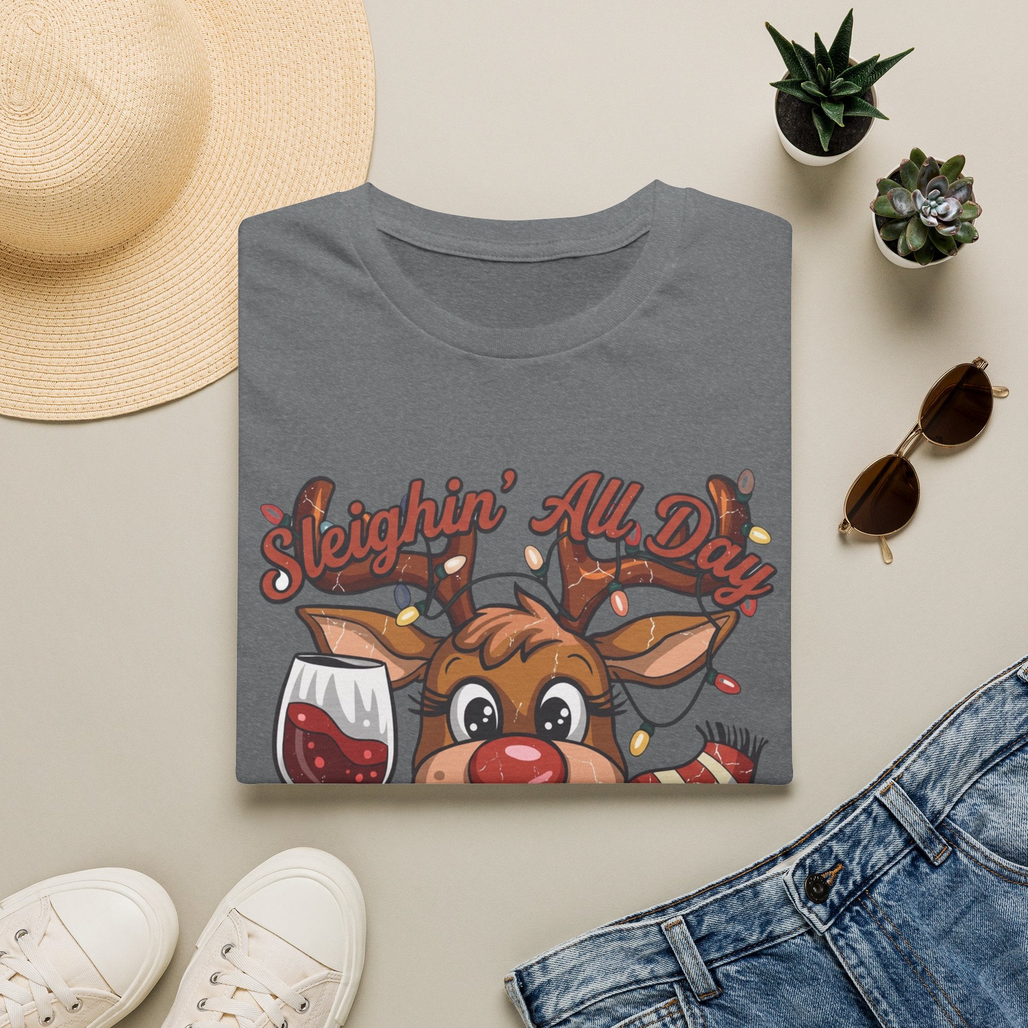 Reindeer Sleighin' All Day Tipsy All Night print on a Graphite Heather t-shirt, folded beside a straw hat and jeans