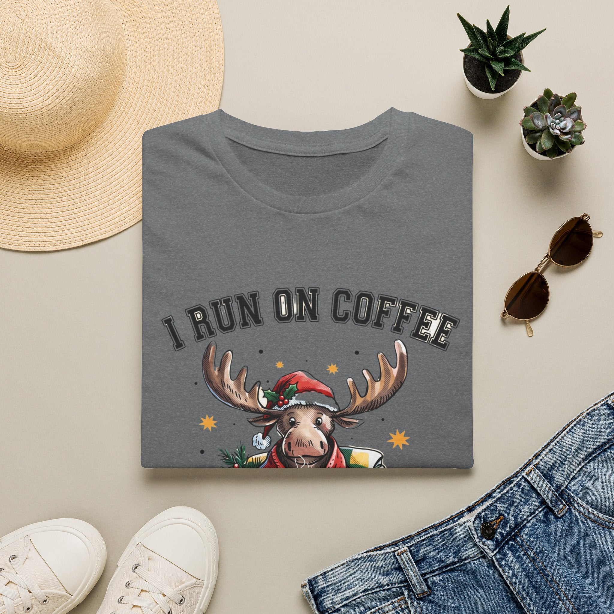 Moose I Run On Coffee and Sleighin' It print on a Graphite Heather t-shirt, folded beside a straw hat and jeans