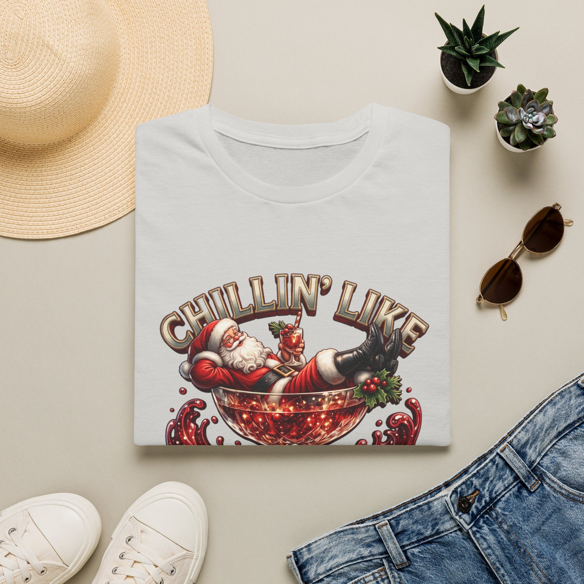 Chillin' Like a Kringle Santa print on an Ice Grey t-shirt, folded beside a straw hat and jeans