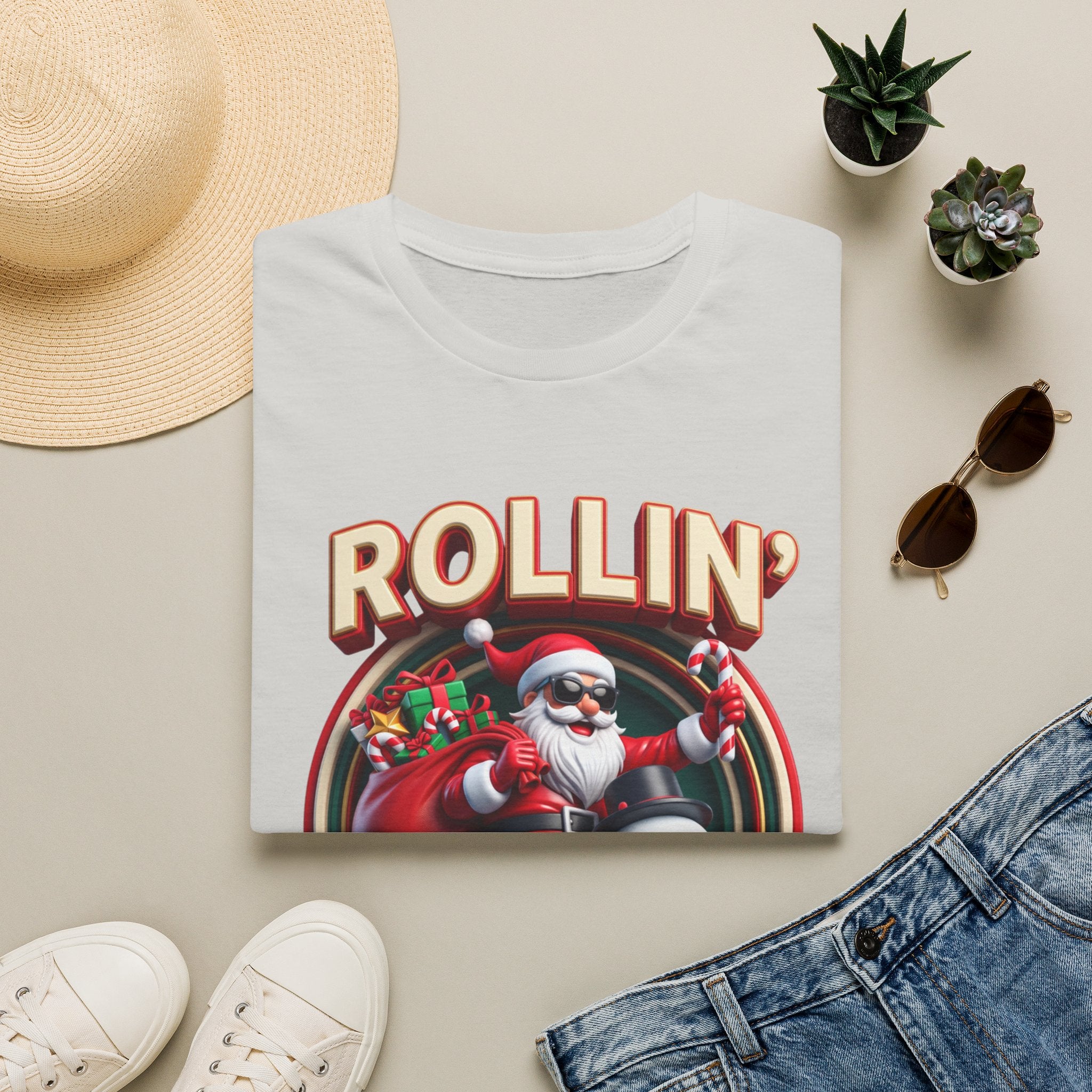 Rollin' with My Snowmies Santa & Snowman print on an Ice Grey t-shirt, folded beside a straw hat and jeans