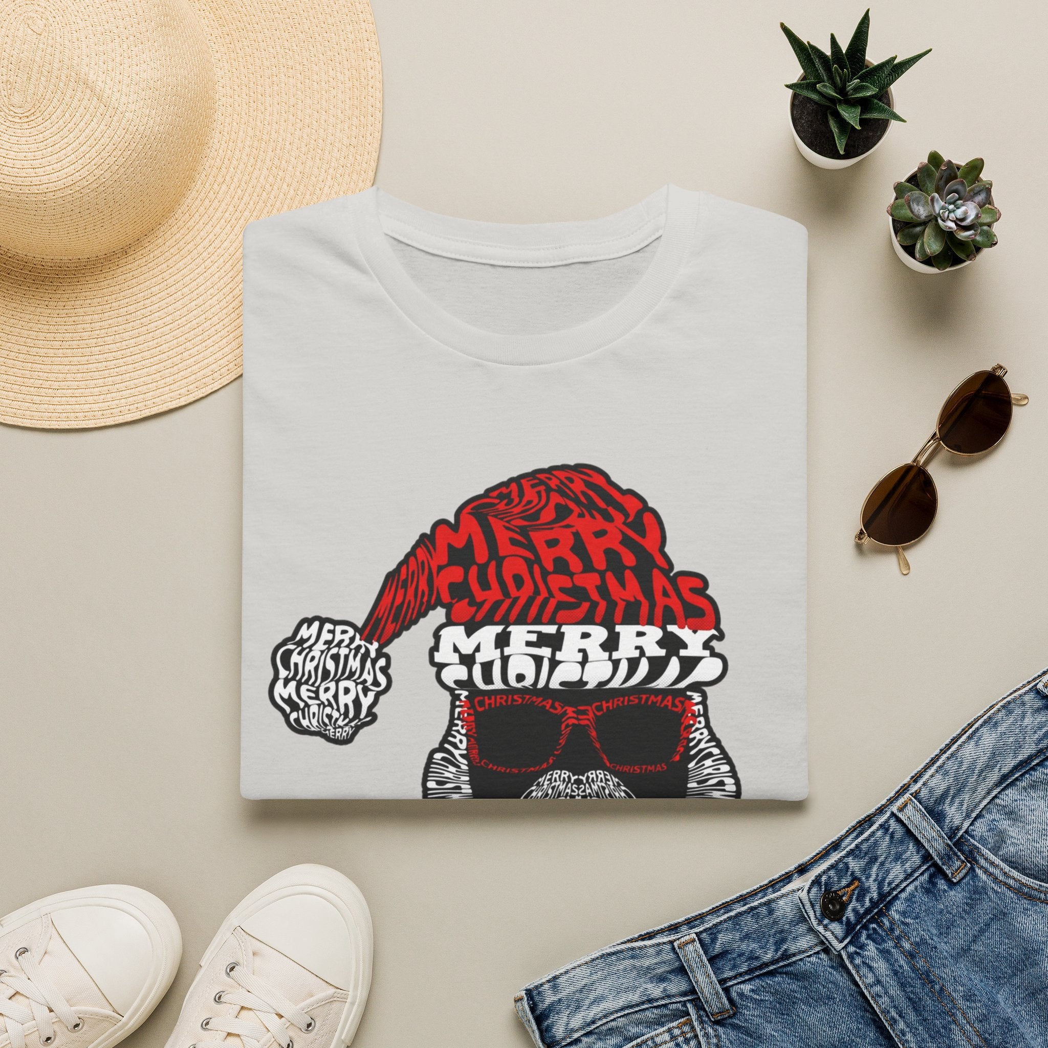 Cool Santa Sunglasses Typography Merry print on an Ice Grey t-shirt, folded beside a straw hat and jeans