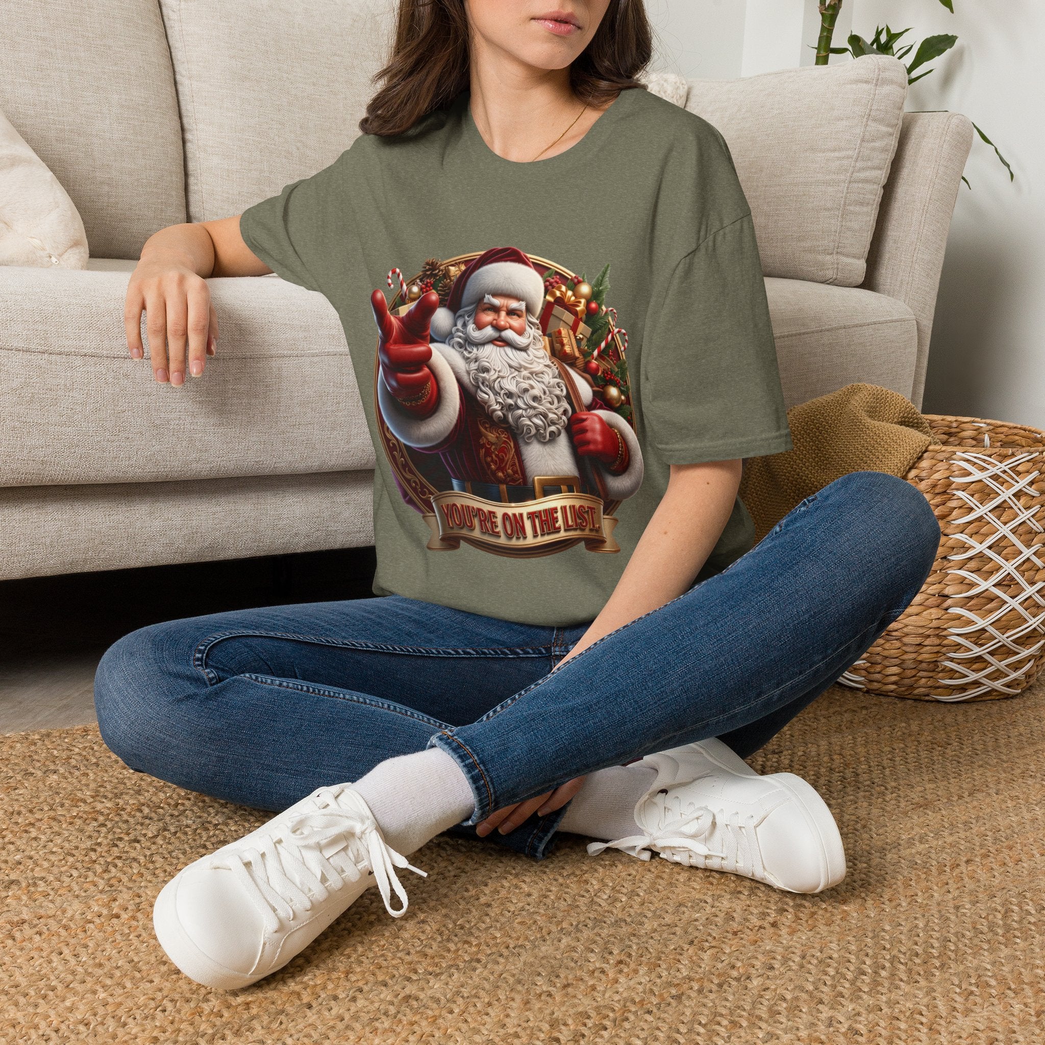 Santa You're On The List Pointing t-shirt in Heather Military Green, worn by a woman seated on a rug