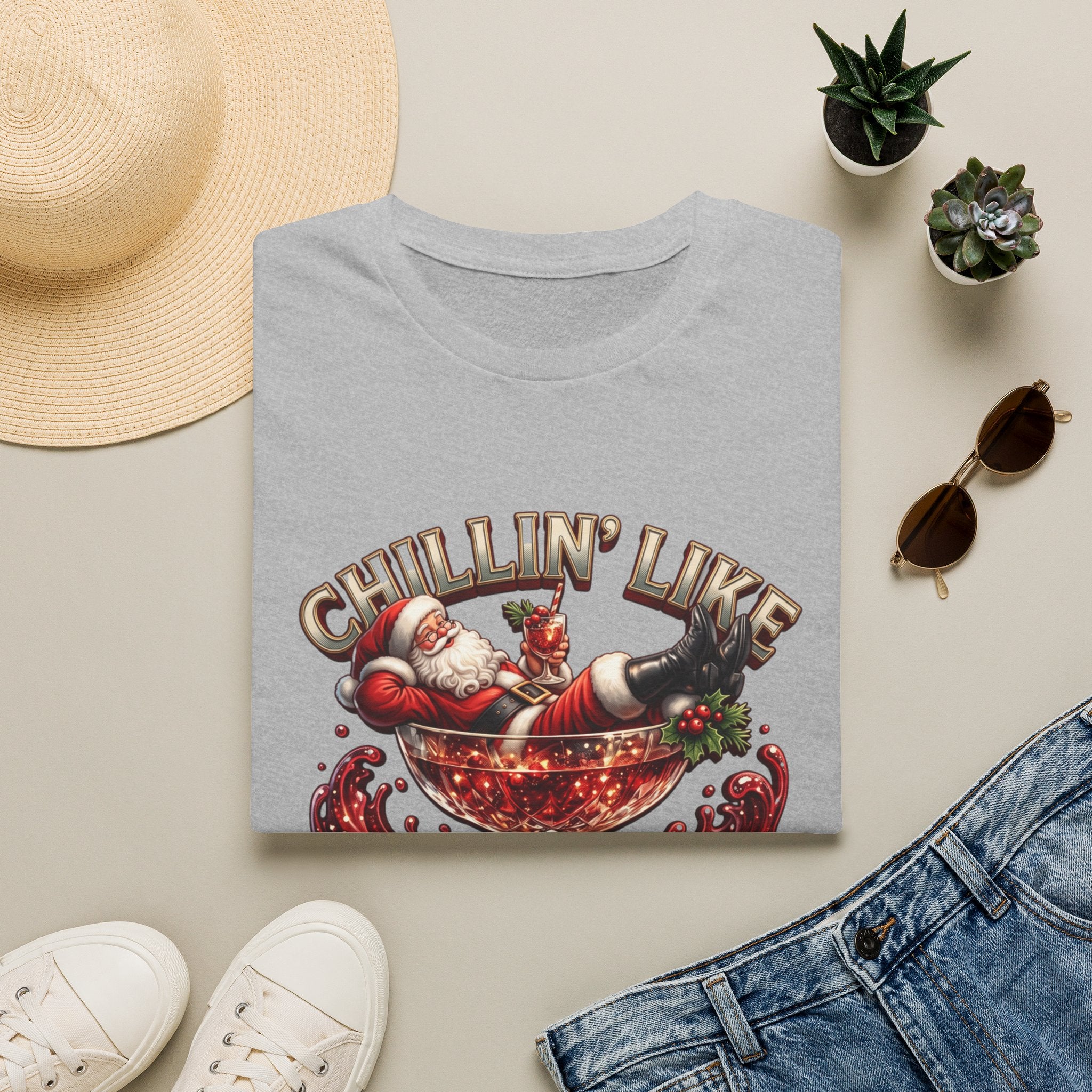 Chillin' Like a Kringle Santa print on a Sport Grey t-shirt, folded beside a straw hat and jeans