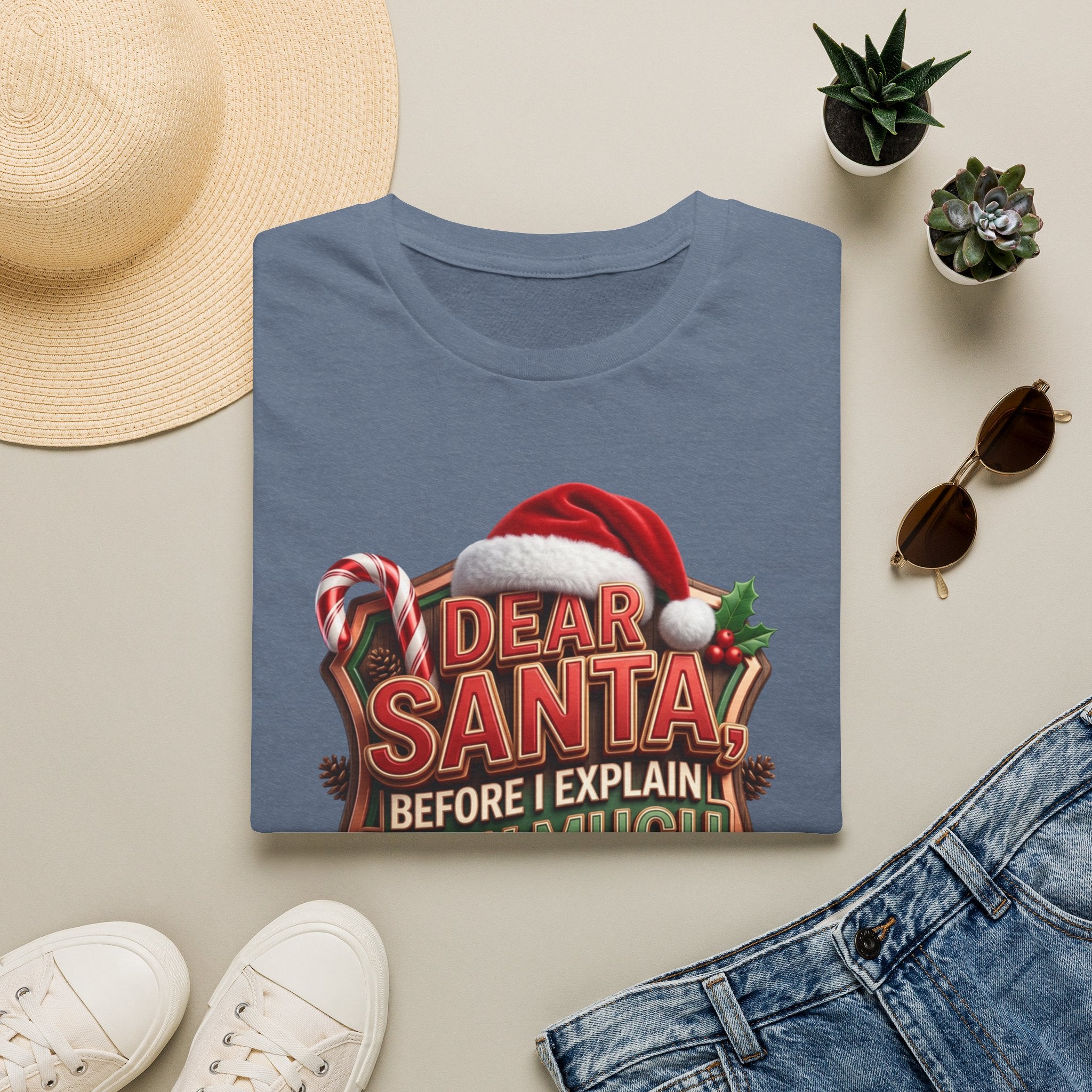 Dear Santa Before I Explain print on a Heather Indigo t-shirt, folded beside a straw hat and jeans