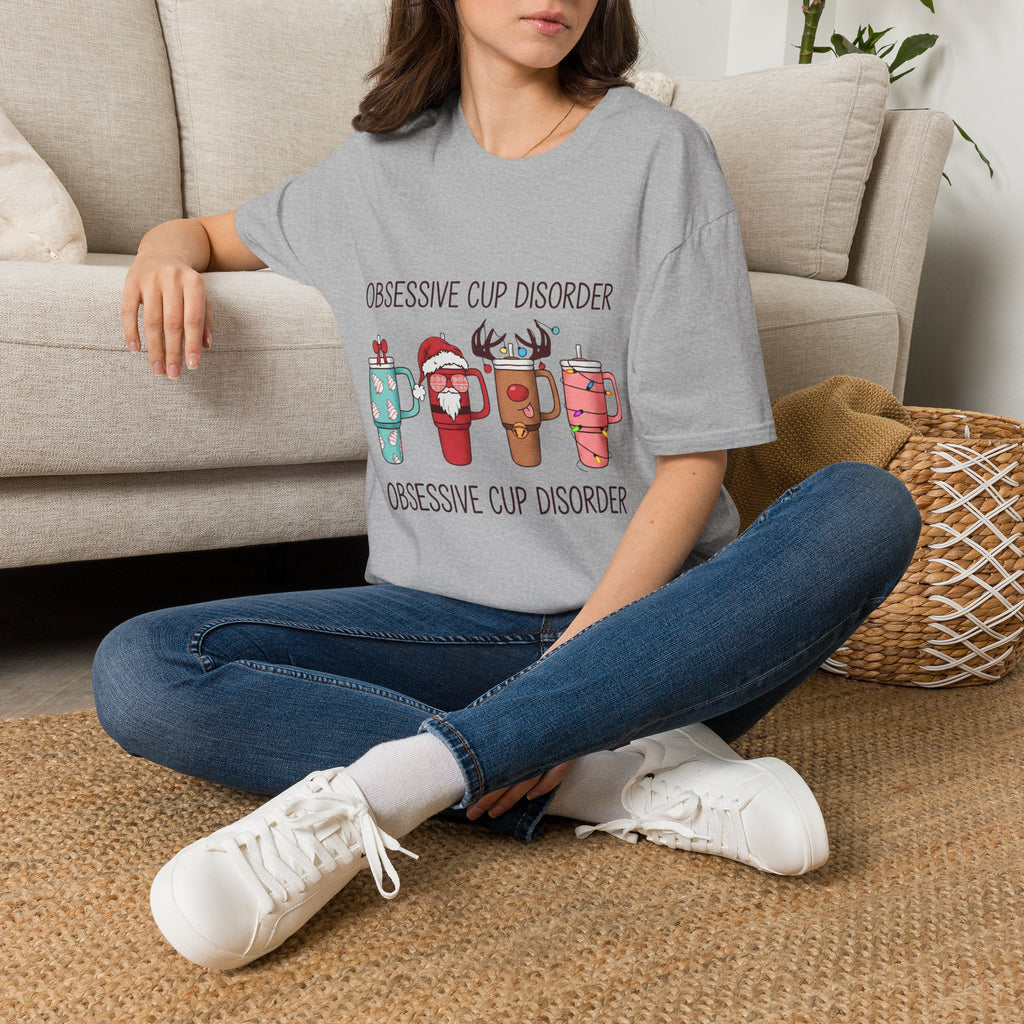 Obsessive Cup Disorder Funny Christmas Tumbler t-shirt in Sport Grey, worn by a woman seated on a rug