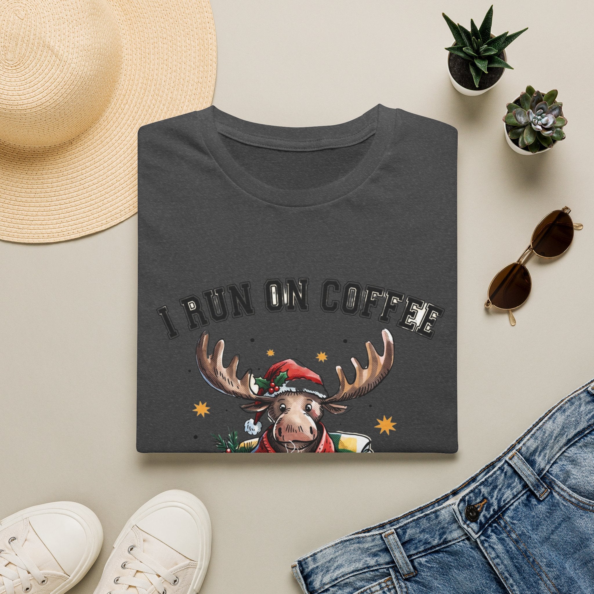 Moose I Run On Coffee and Sleighin' It print on a Dark Heather t-shirt, folded beside a straw hat and jeans