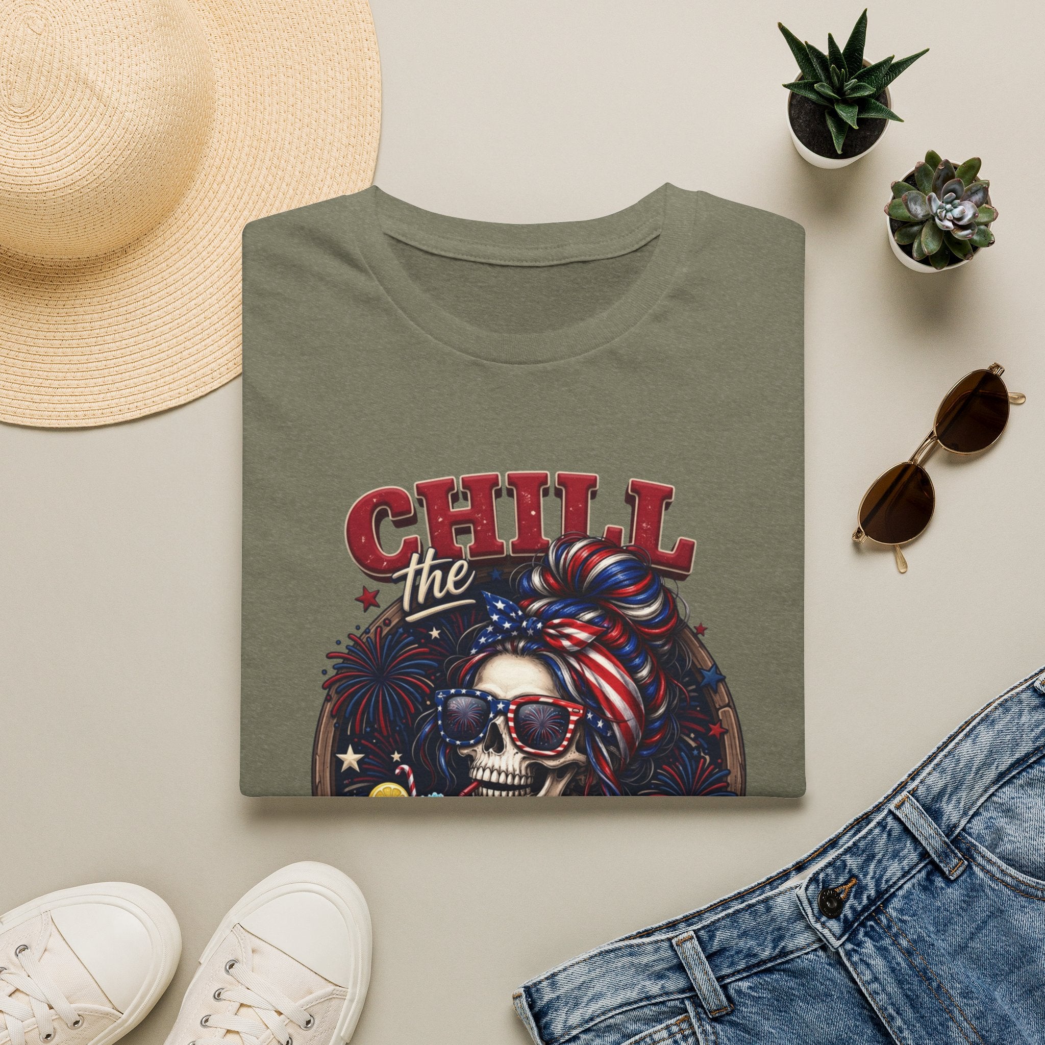 Chill the Fourth Out Patriotic Skeleton 4th of July print on a Heather Military Green t-shirt, folded beside a straw hat…