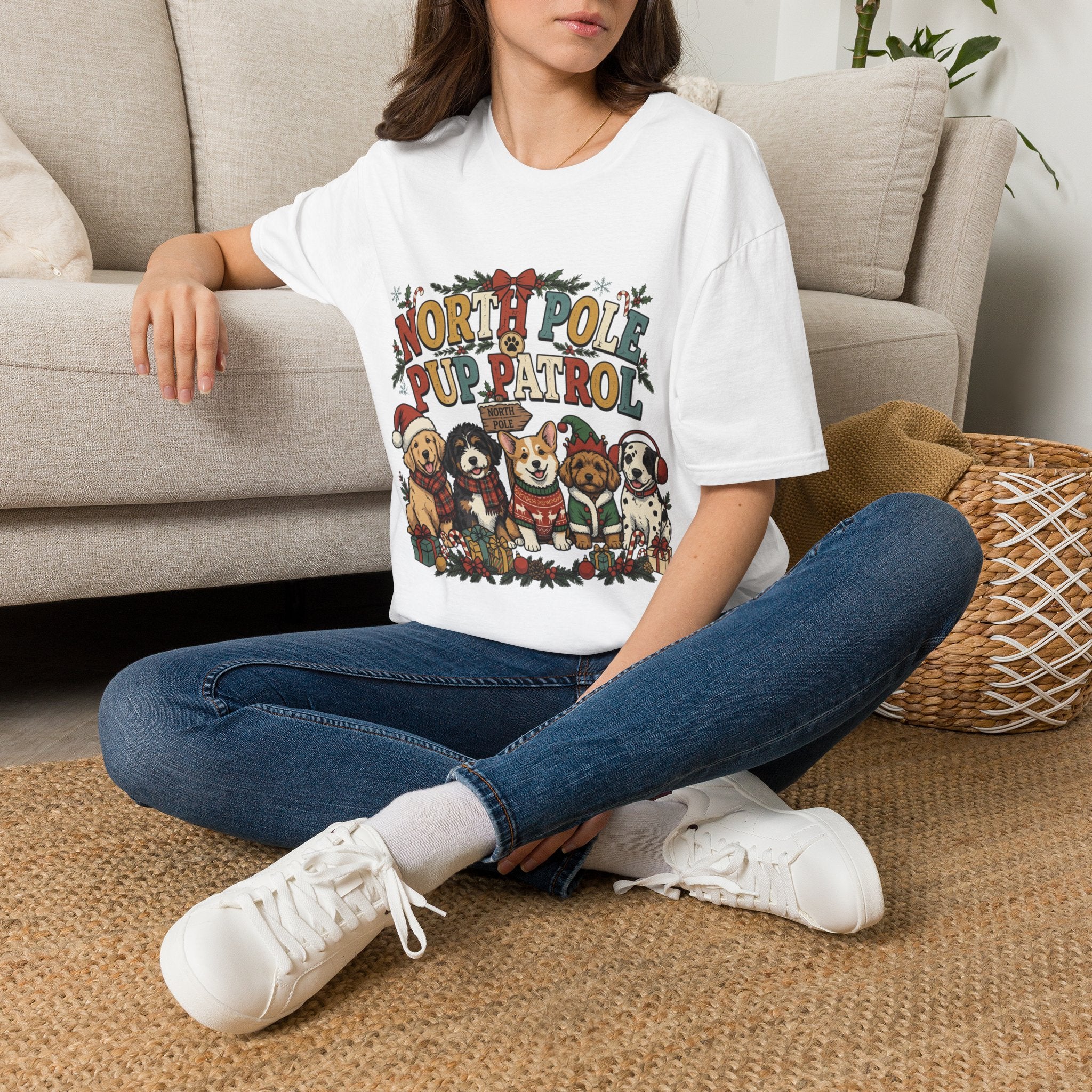 North Pole Pup Patrol Christmas Dogs t-shirt in White, worn by a woman seated on a rug