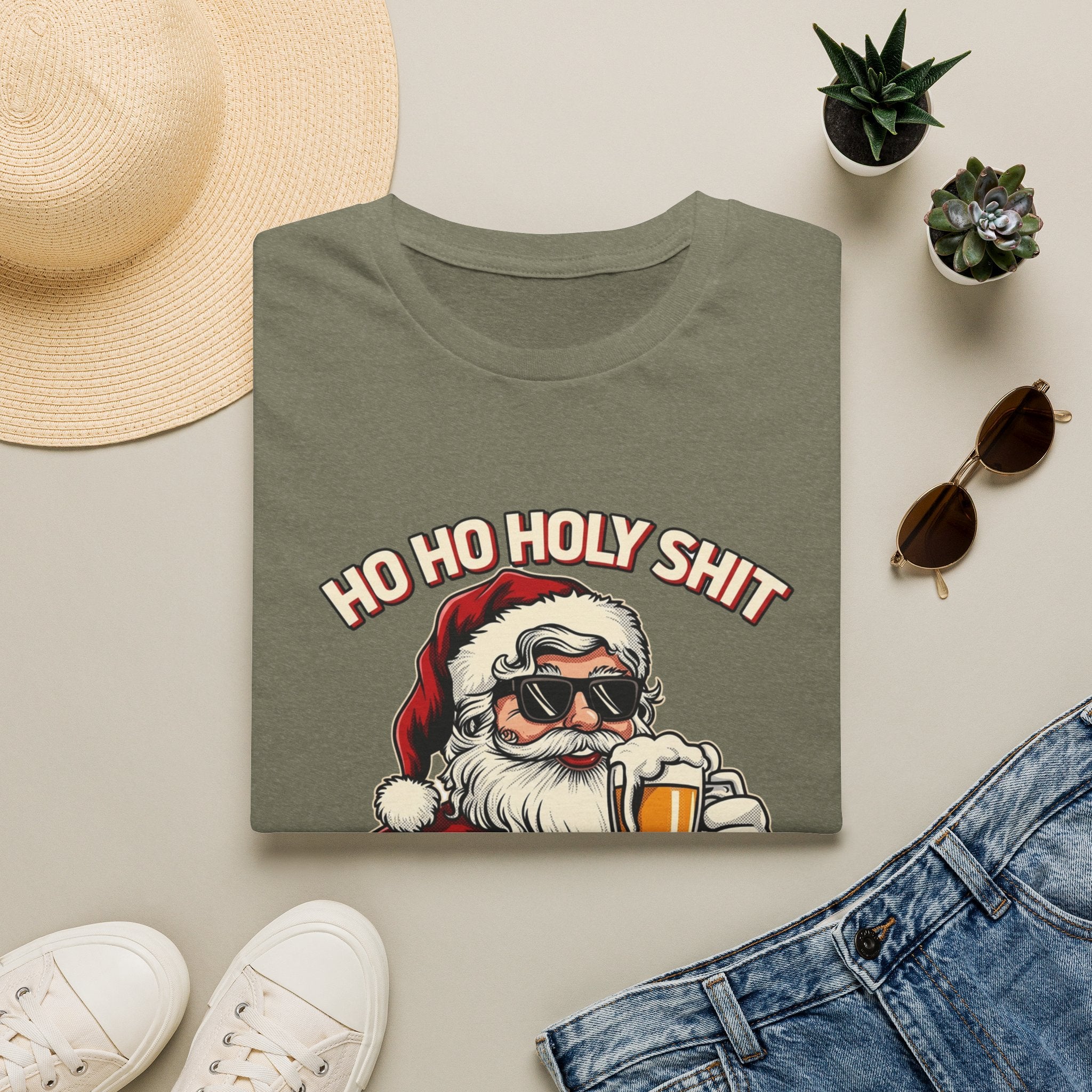 Ho Ho Holy Sh*t I Need a Beer print on a Heather Military Green t-shirt, folded beside a straw hat and jeans