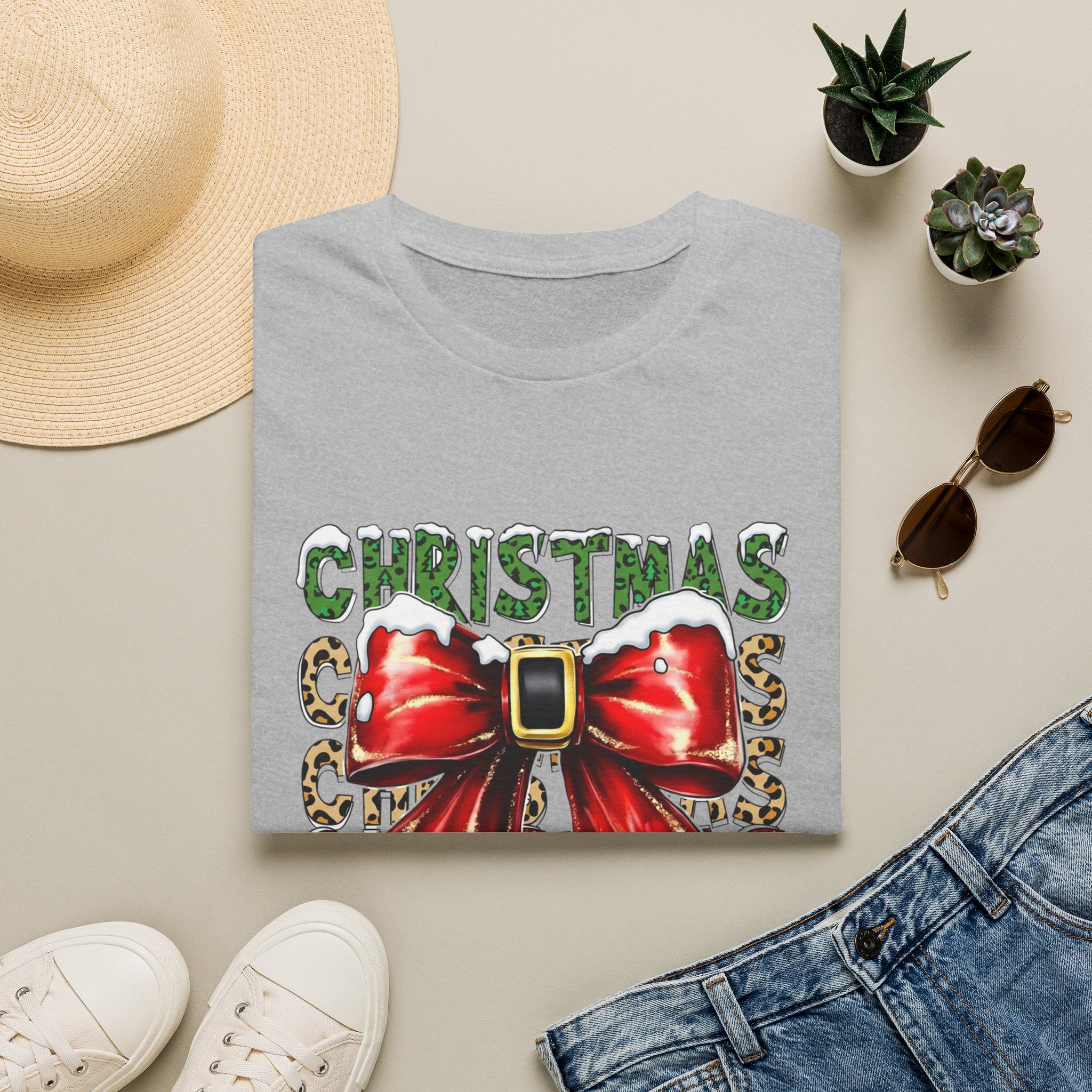 Stacked Christmas Leopard Print Santa Belt Bow print on a Sport Grey t-shirt, folded beside a straw hat and jeans