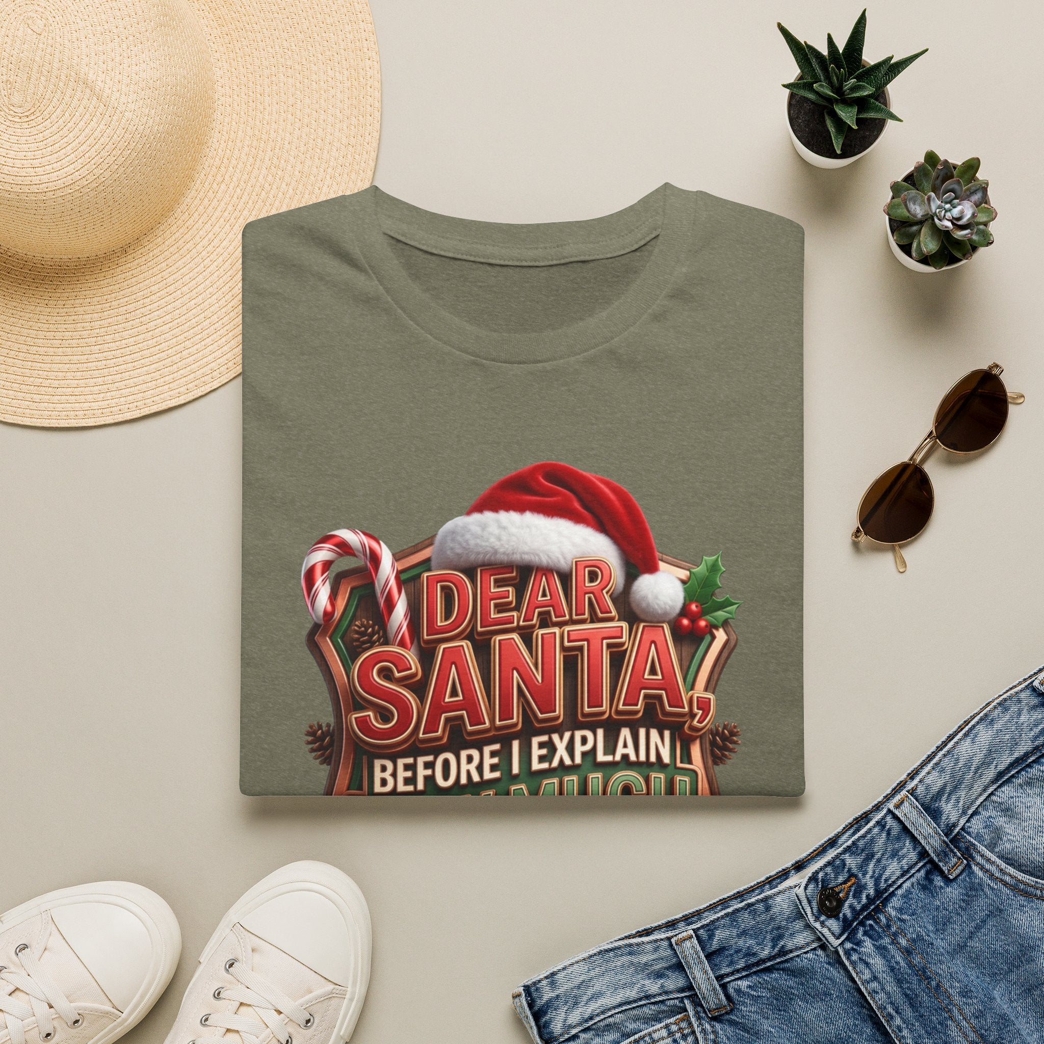 Dear Santa Before I Explain print on a Heather Military Green t-shirt, folded beside a straw hat and jeans