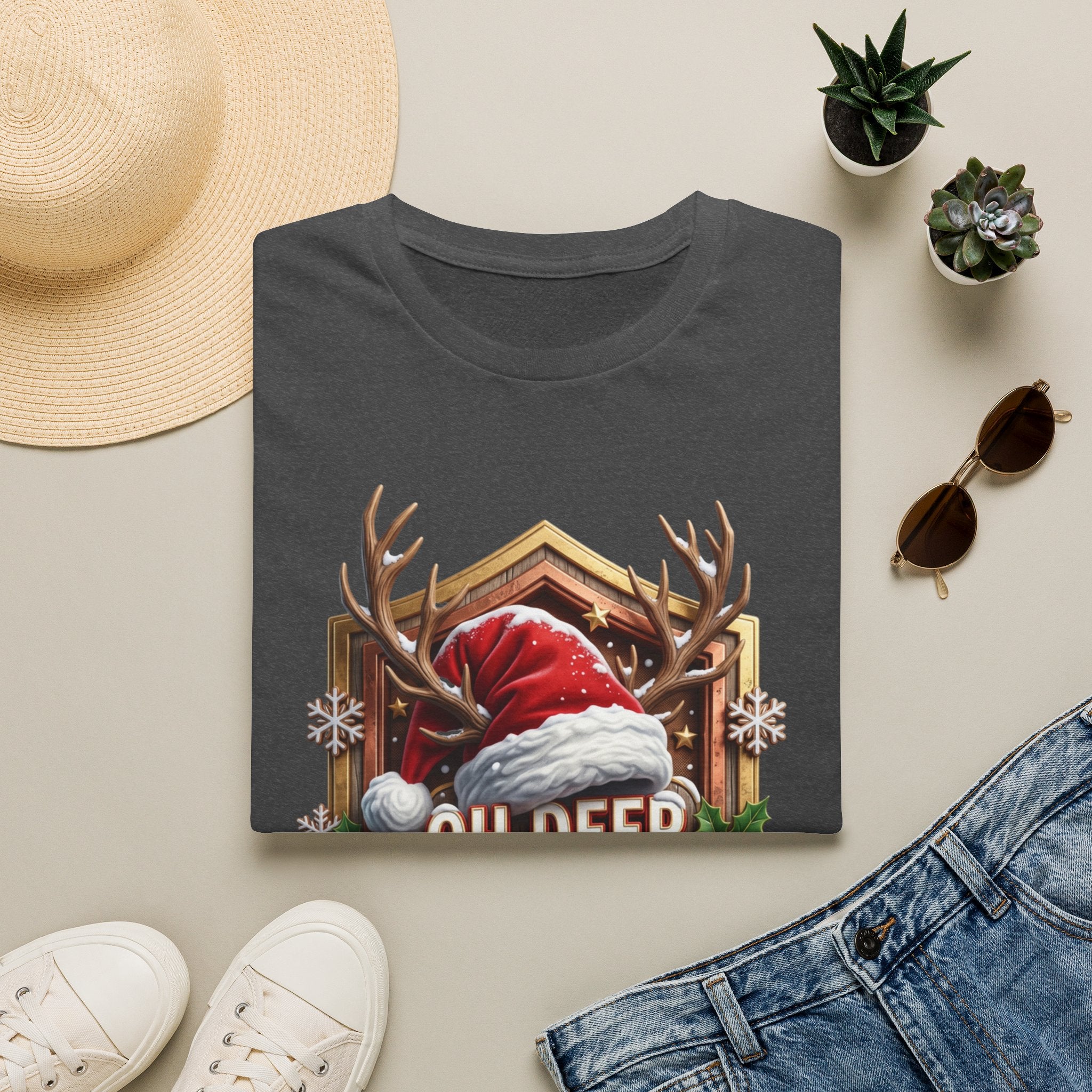 Oh Deer It's Christmas Looks a Lot Like Cocktails print on a Dark Heather t-shirt, folded beside a straw hat and jeans