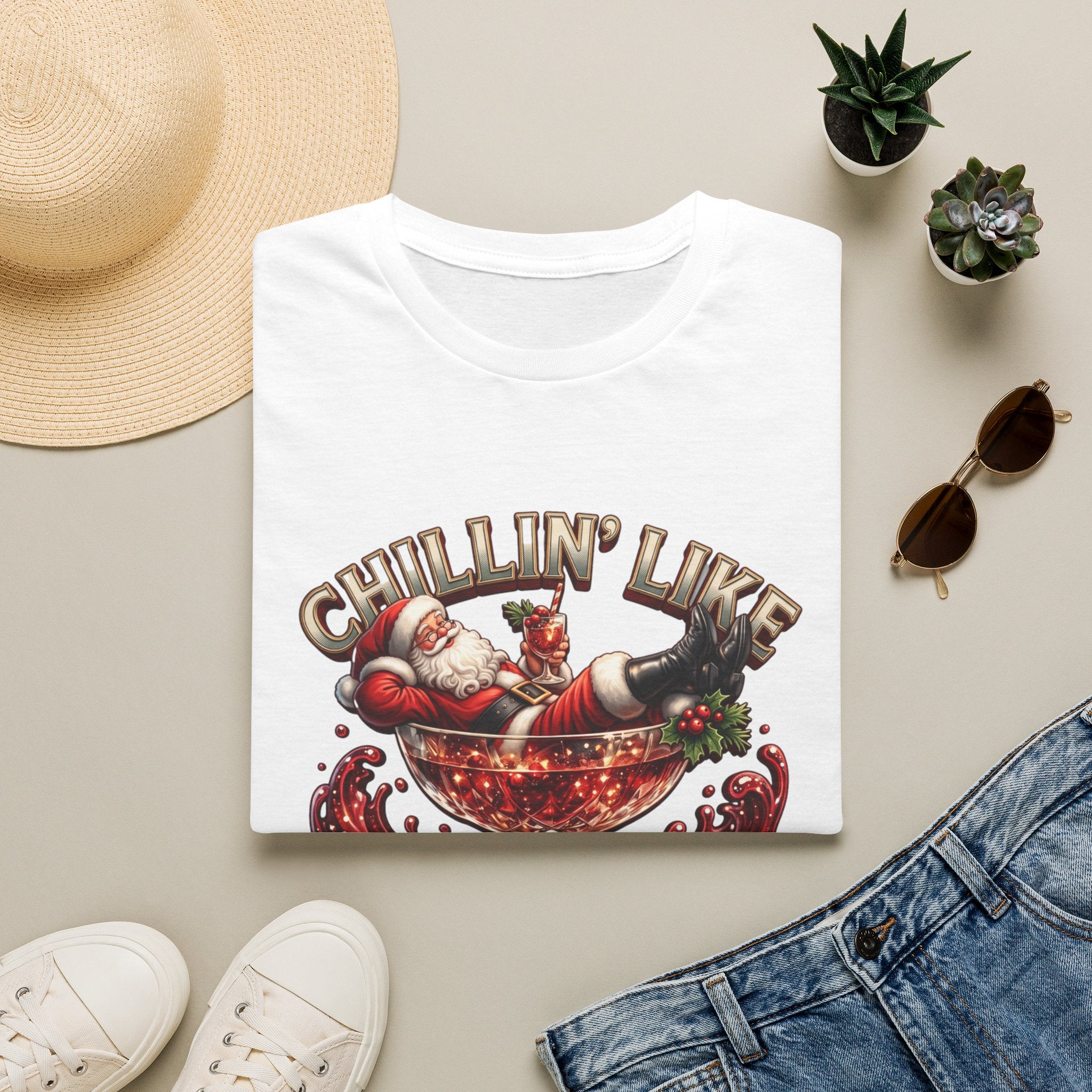 Chillin' Like a Kringle Santa print on a White t-shirt, folded beside a straw hat and jeans