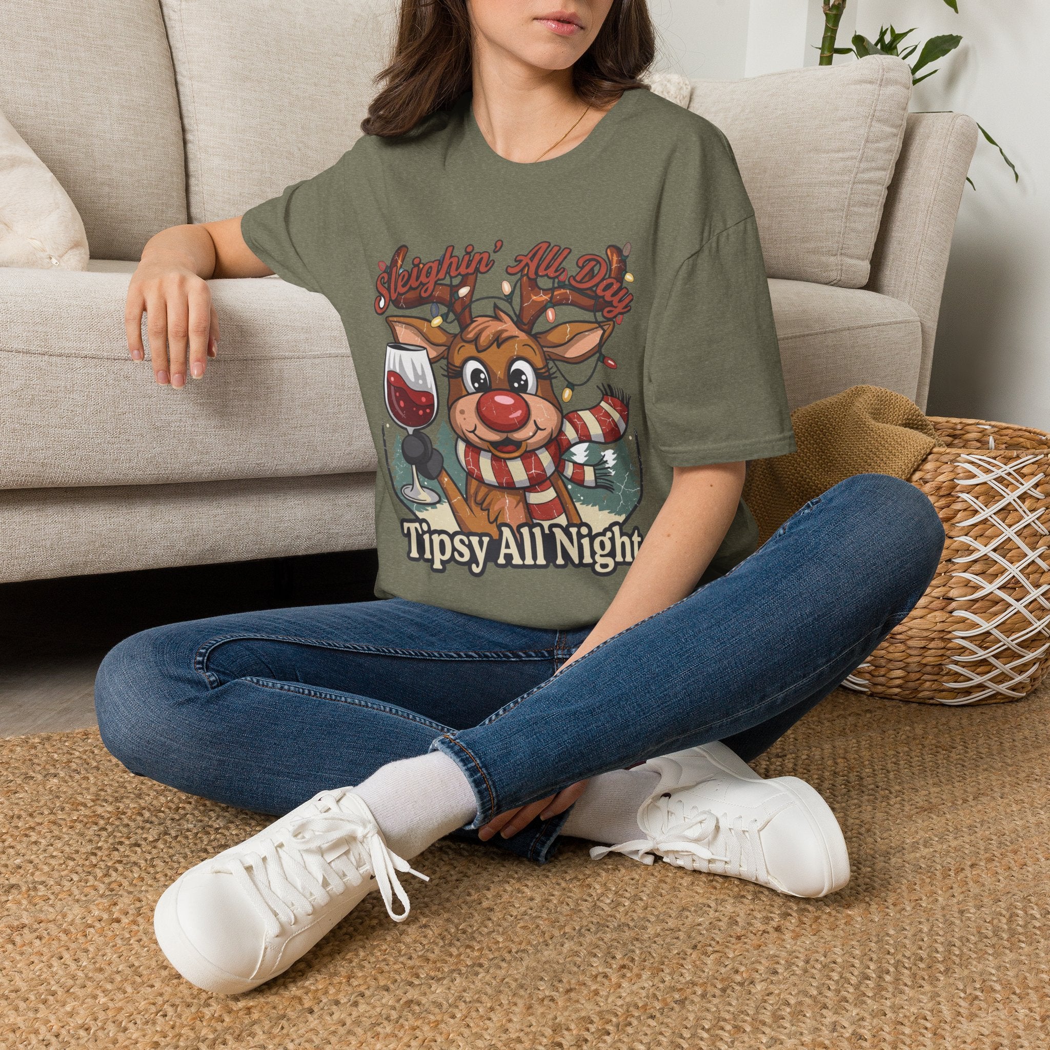 Reindeer Sleighin' All Day Tipsy All Night t-shirt in Heather Military Green, worn by a woman seated on a rug