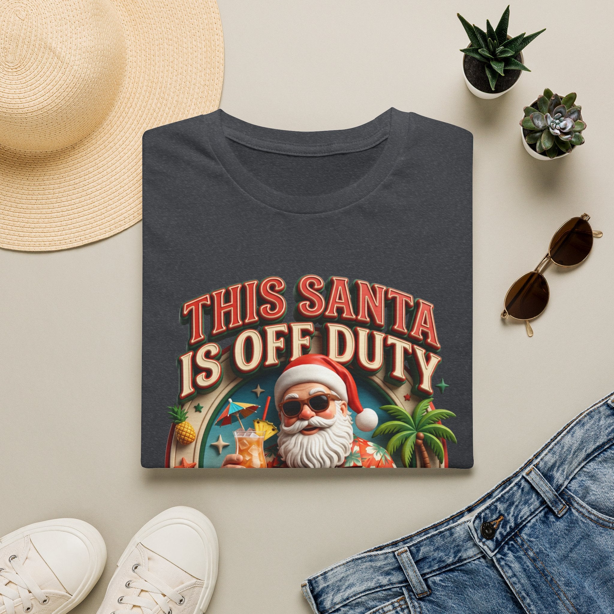 This Santa Is Off Duty Cocktail Club print on a Dark Heather Grey t-shirt, folded beside a straw hat and jeans