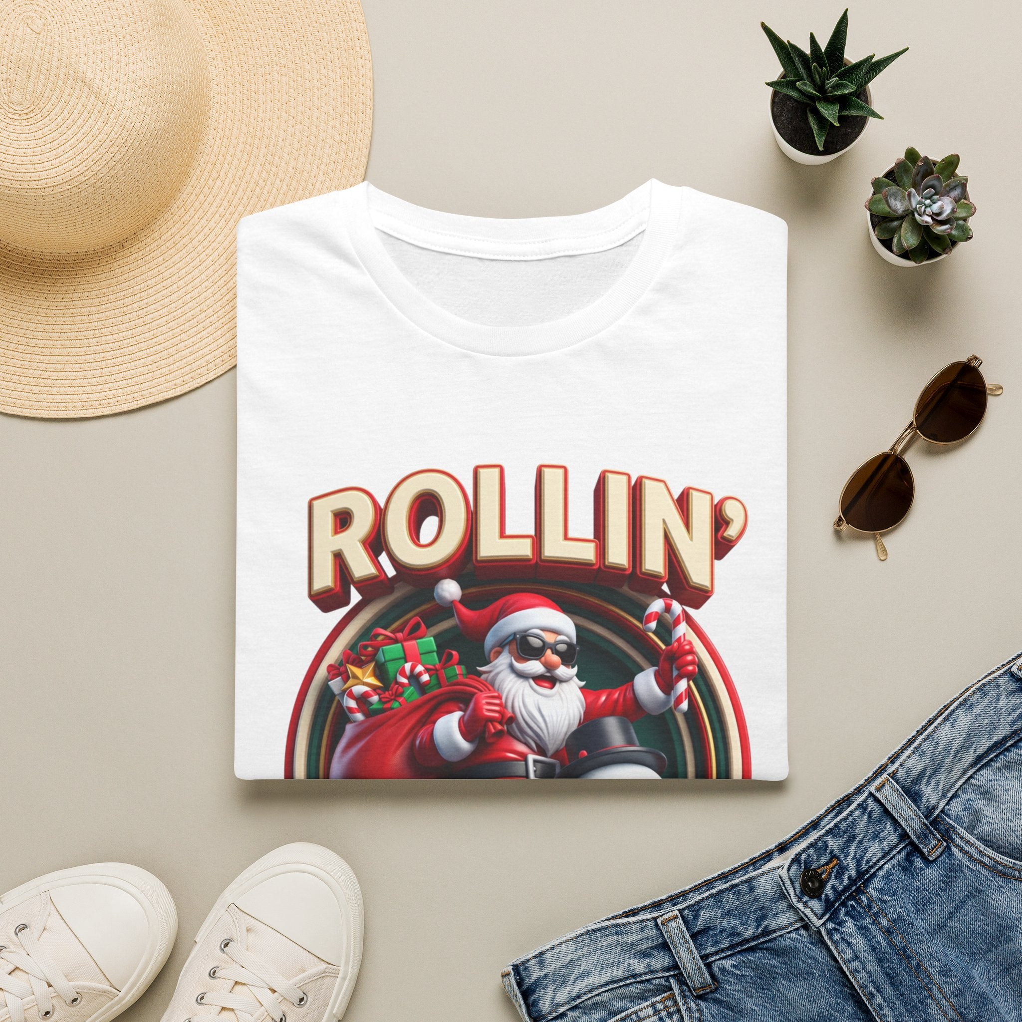 Rollin' with My Snowmies Santa & Snowman print on a White t-shirt, folded beside a straw hat and jeans