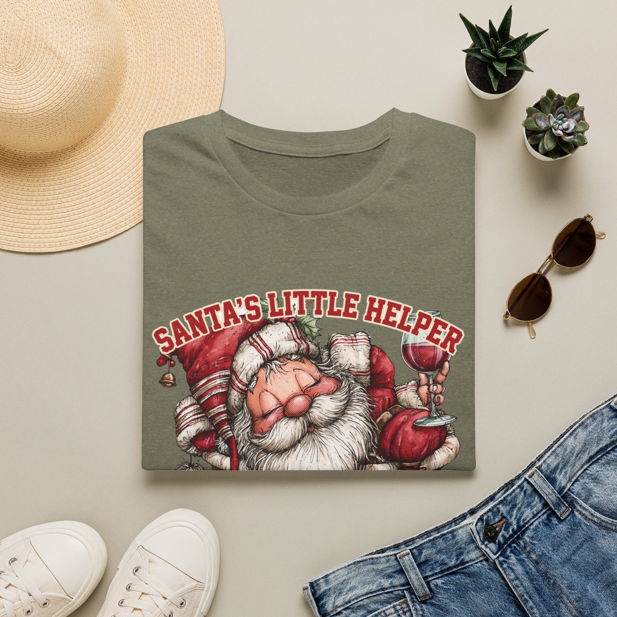 Santa's Little Helper Is Lit Christmas Wine print on a Heather Military Green t-shirt, folded beside a straw hat and jeans