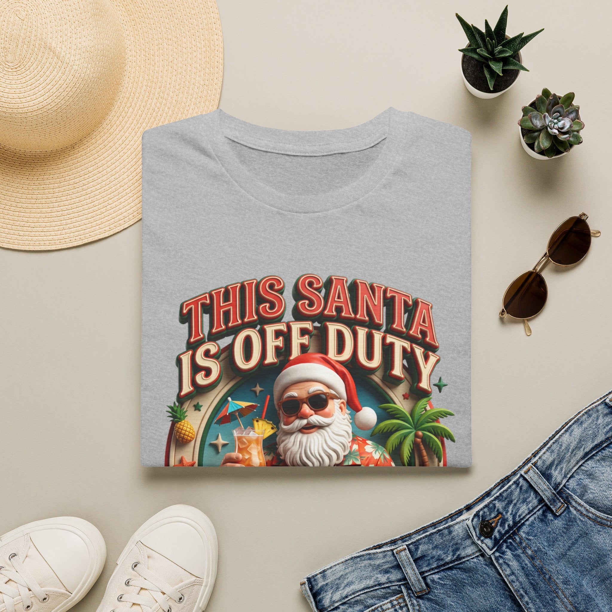This Santa Is Off Duty Cocktail Club print on a Sport Grey t-shirt, folded beside a straw hat and jeans