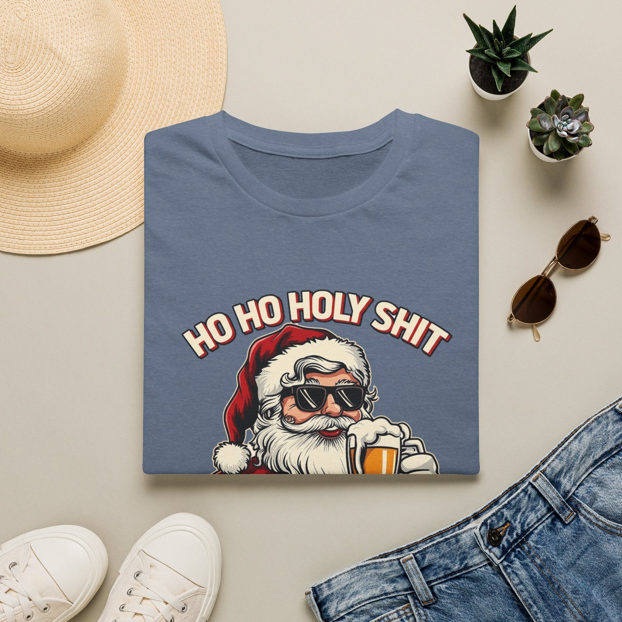Ho Ho Holy Sh*t I Need a Beer print on a Heather Indigo t-shirt, folded beside a straw hat and jeans