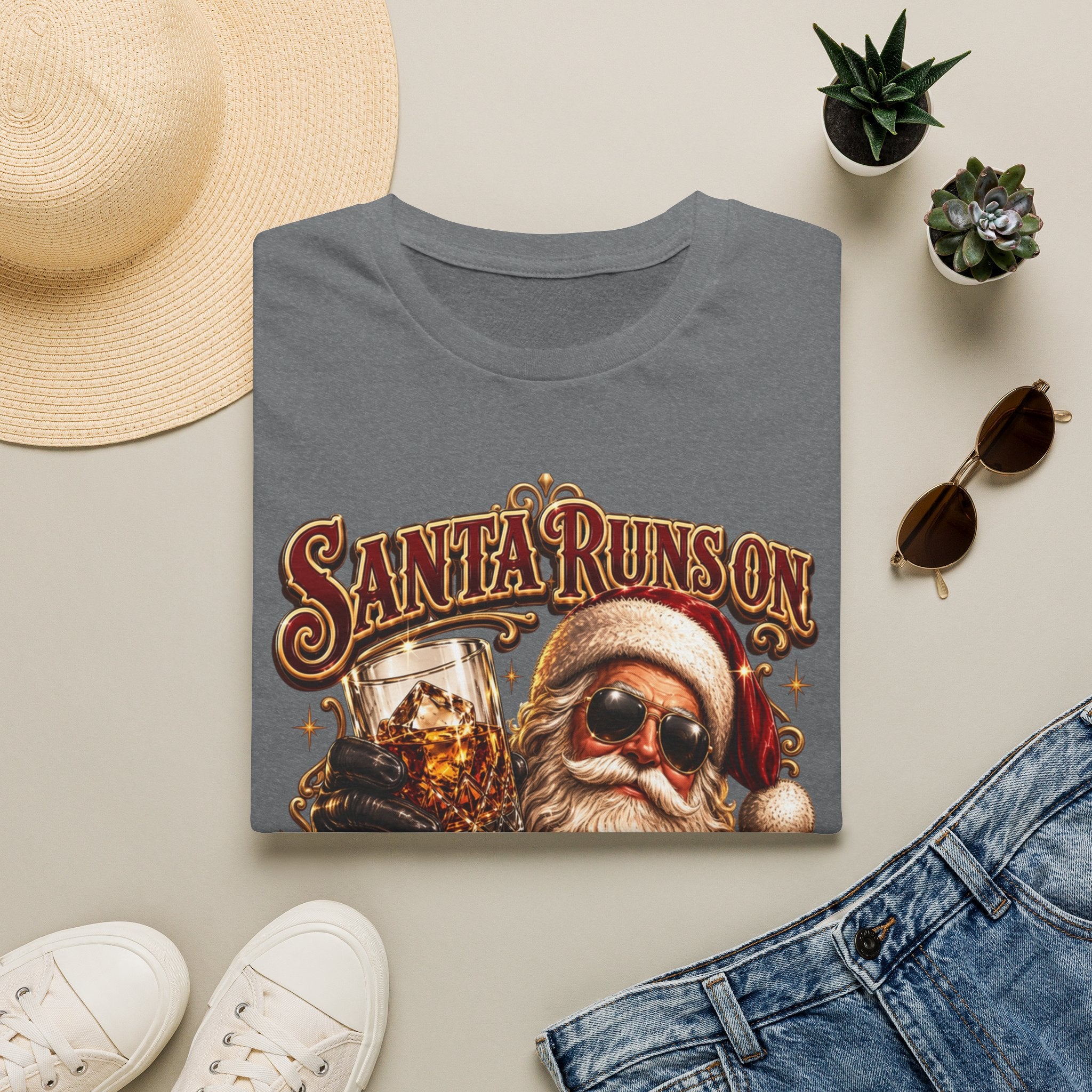 Santa Runs on Bourbon Vintage Whiskey print on a Graphite Heather t-shirt, folded beside a straw hat and jeans