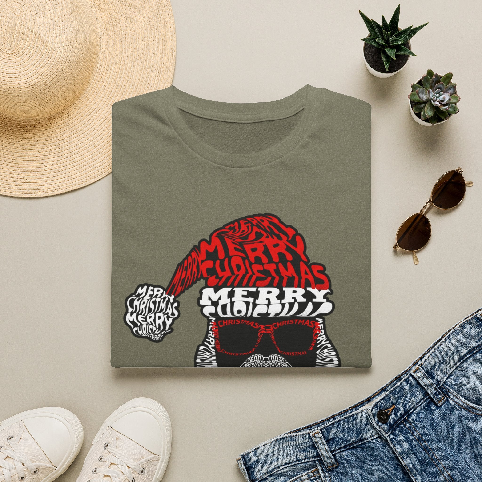 Cool Santa Sunglasses Typography Merry print on a Heather Military Green t-shirt, folded beside a straw hat and jeans