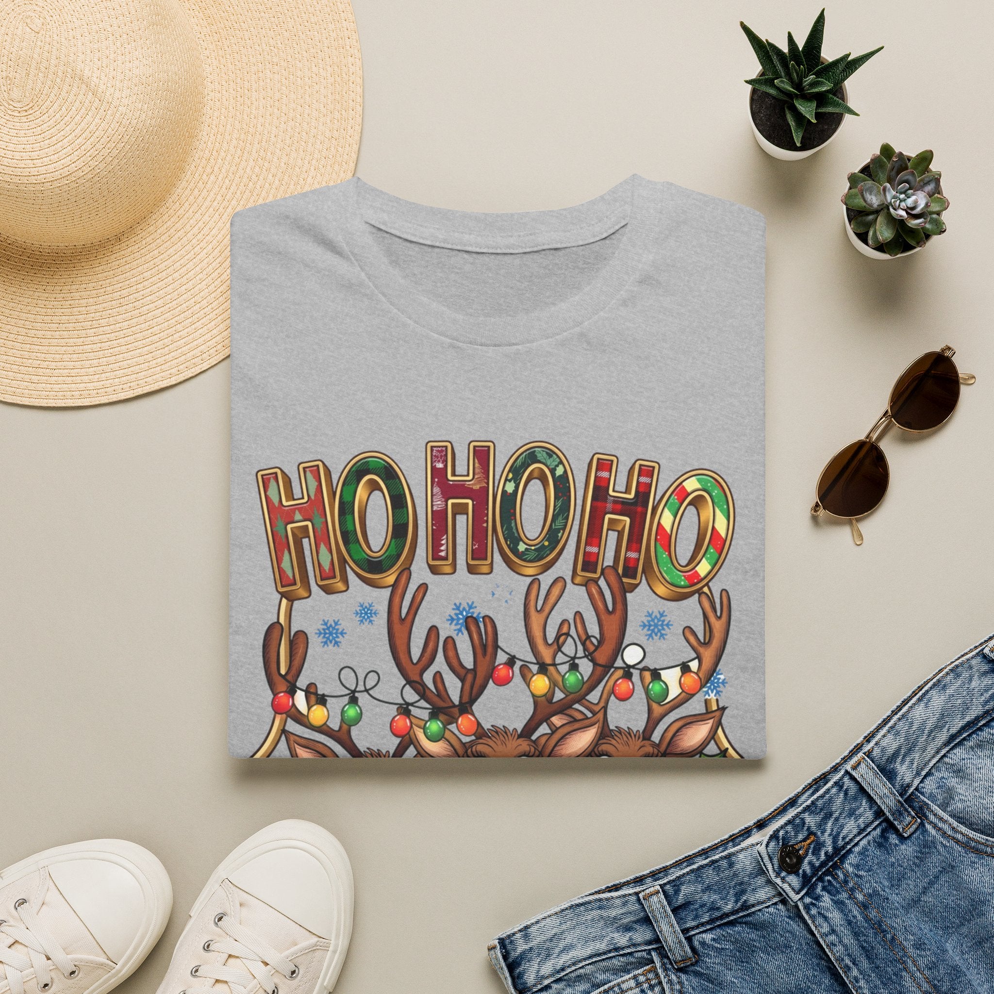 Reindeer Trio Ho Ho Ho Christmas Lights print on a Sport Grey t-shirt, folded beside a straw hat and jeans