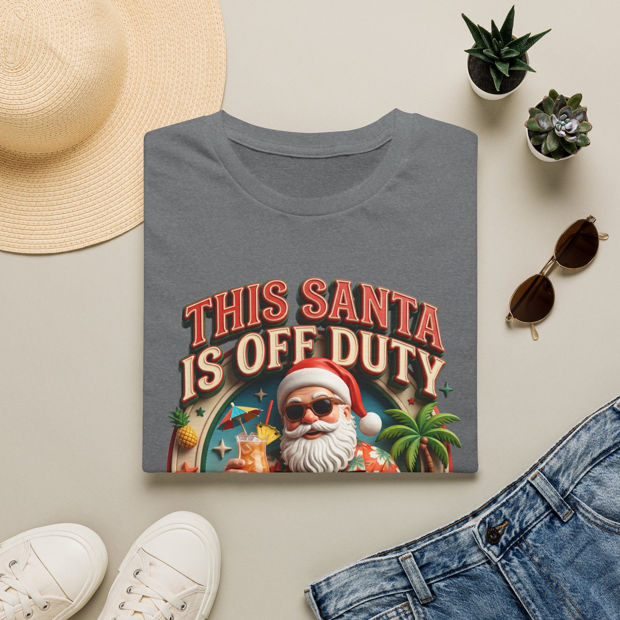 This Santa Is Off Duty Cocktail Club print on a Graphite Heather t-shirt, folded beside a straw hat and jeans