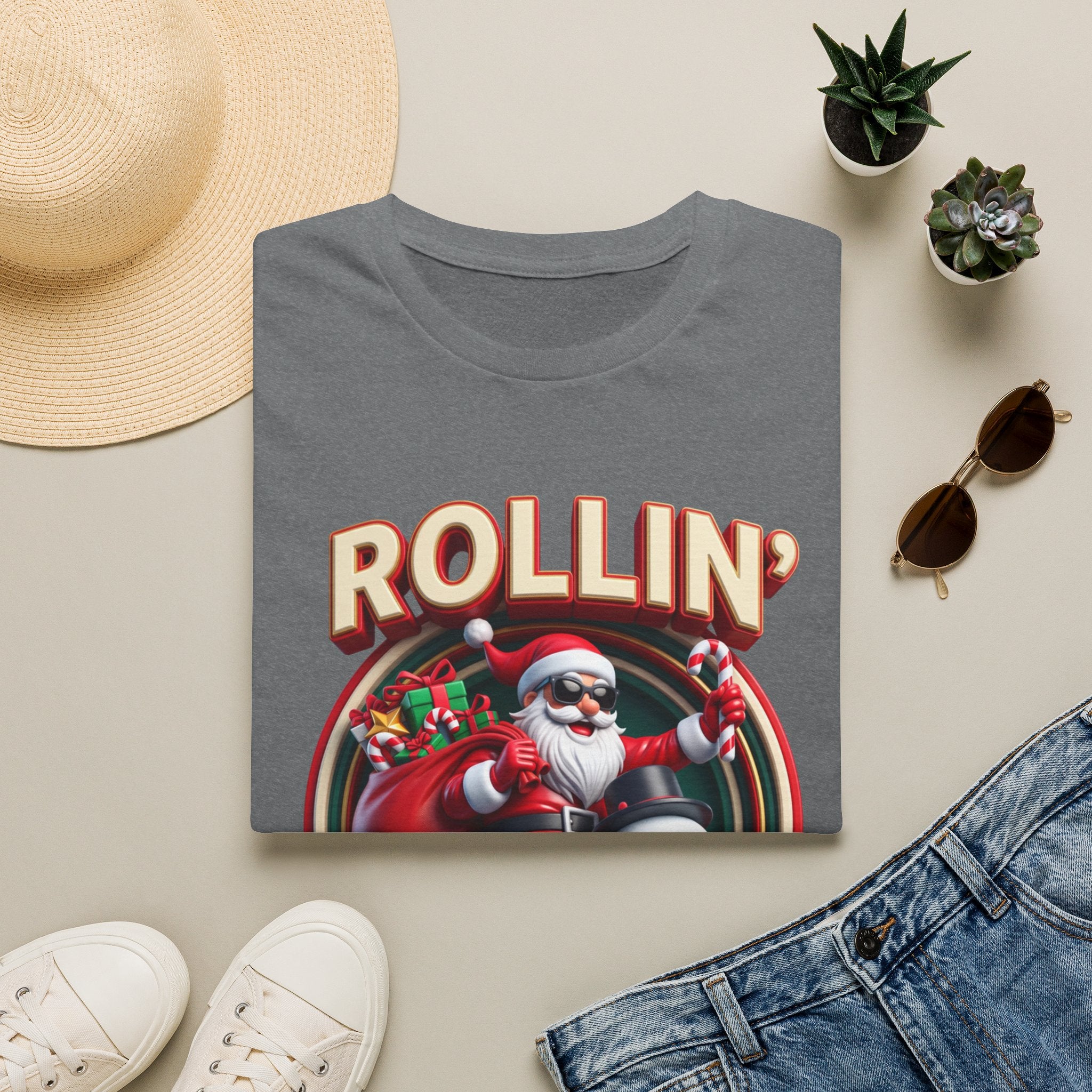 Rollin' with My Snowmies Santa & Snowman print on a Graphite Heather t-shirt, folded beside a straw hat and jeans