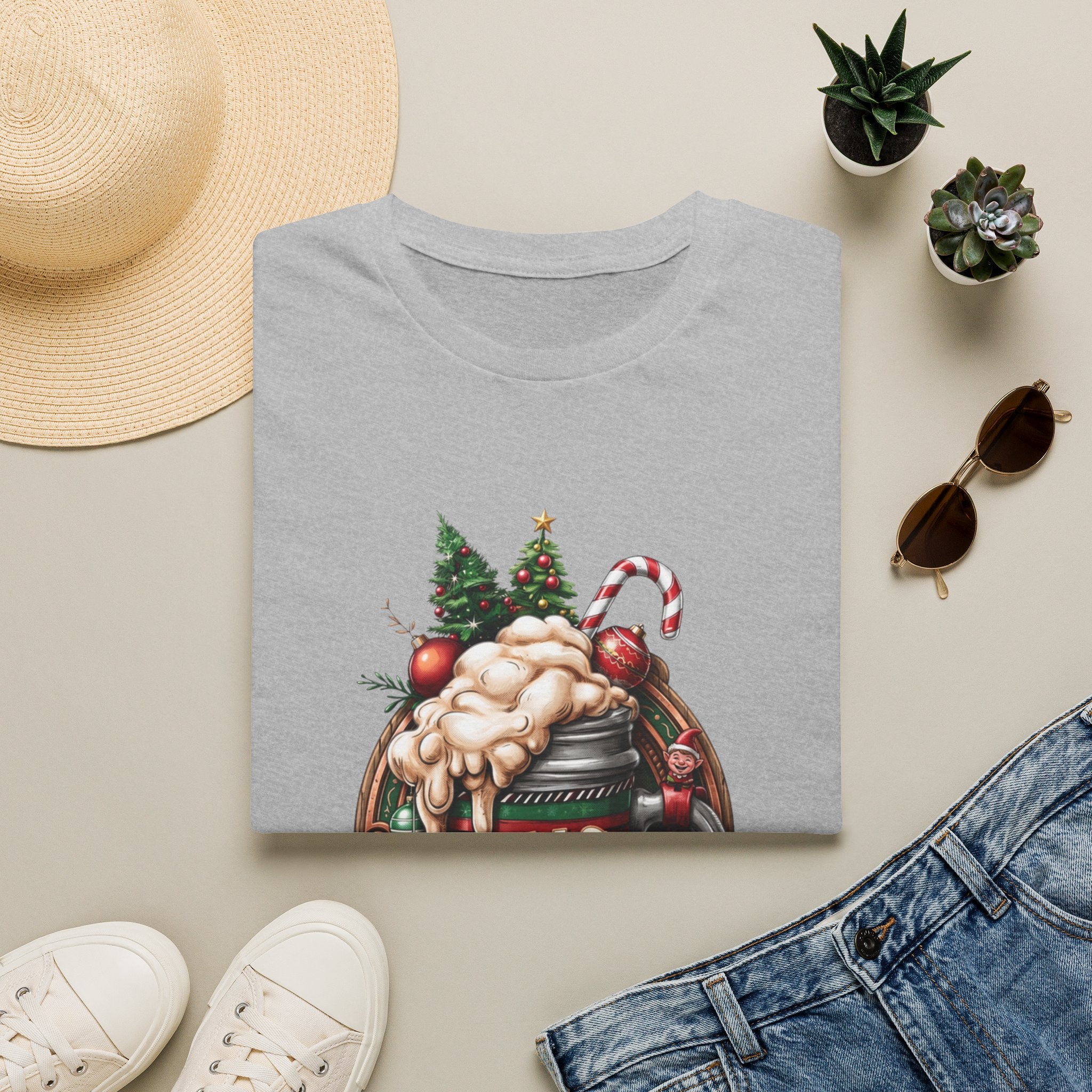XMAS Beer Pour Me a Very Merry Christmas print on a Sport Grey t-shirt, folded beside a straw hat and jeans