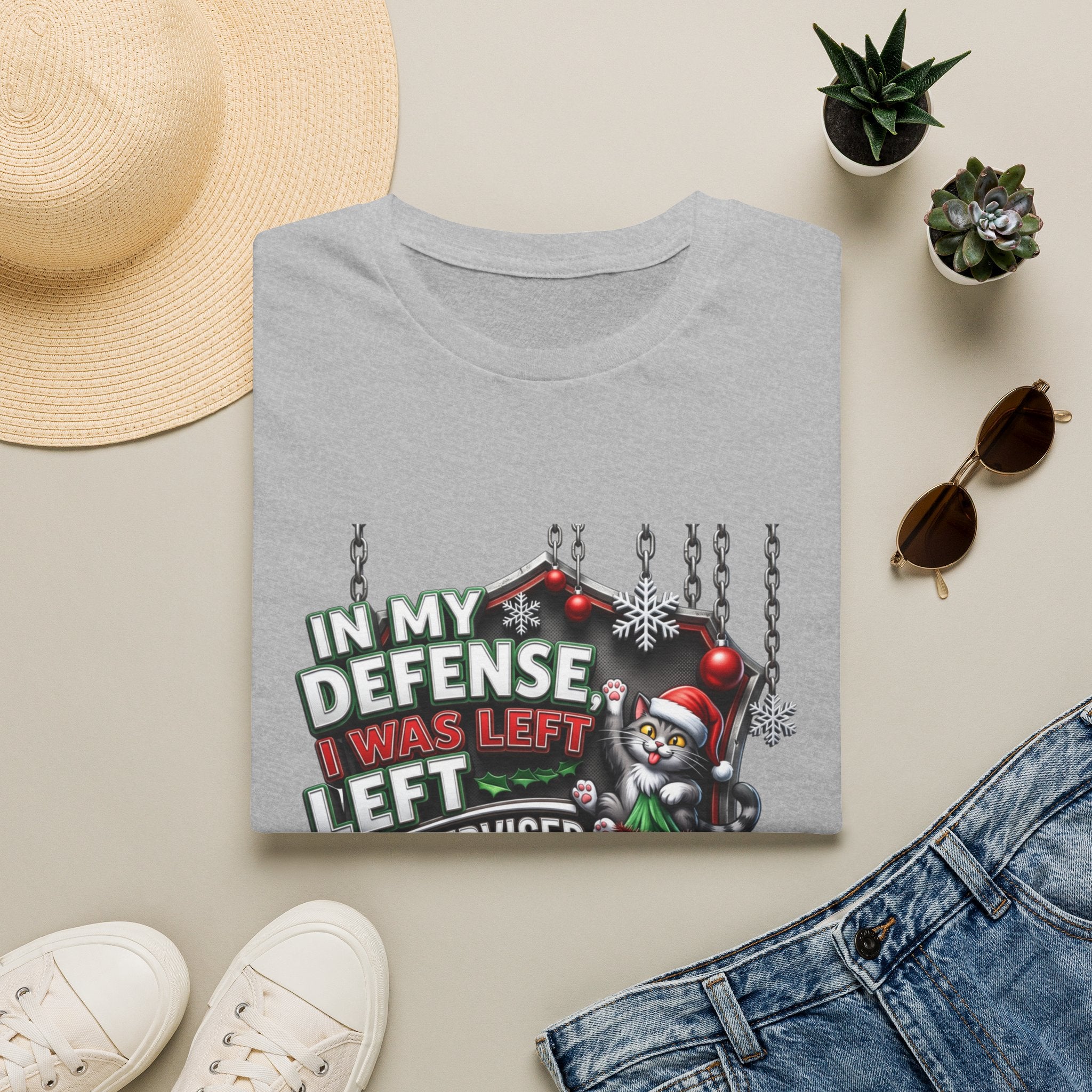 Cat In My Defense Left Unsupervised print on a Sport Grey t-shirt, folded beside a straw hat and jeans