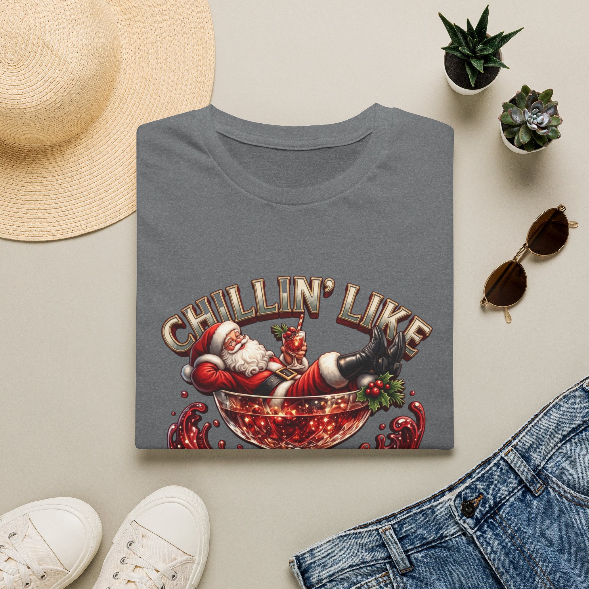 Chillin' Like a Kringle Santa print on a Graphite Heather t-shirt, folded beside a straw hat and jeans